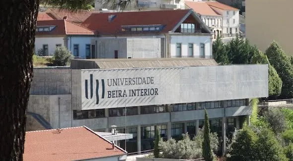 Fachada de um edifício da UBI com o nome Universidade da Beira Interior, entre árvores e telhados.